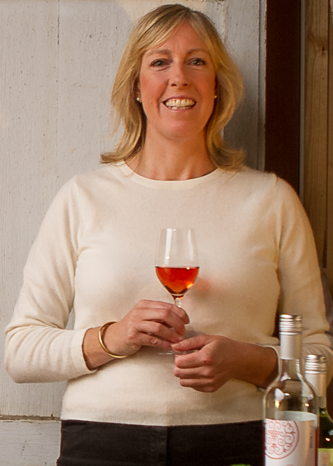 Rebecca Mitchell Wine educator wearing a white jumper and holding a glass of rosé wine next to the bottle. 