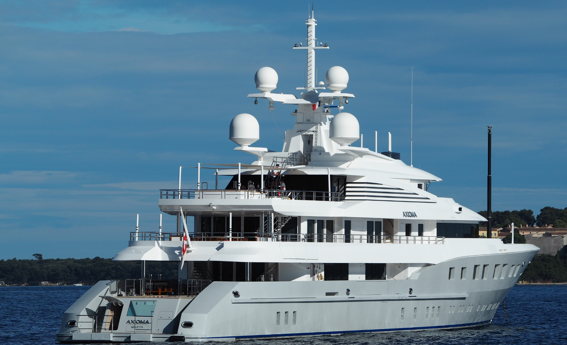 An image of a white super-yacht, with 3 tiers on the ocean with a beautiful blue sky behind.